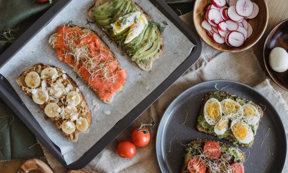 A variety of savory and sweet toasts with avocado, banana, eggs, and fresh toppings on a wooden table.