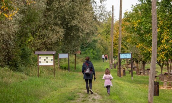 A parent and child walking on a path in a scenic nature reserve in Croatia, surrounded by lush greenery.